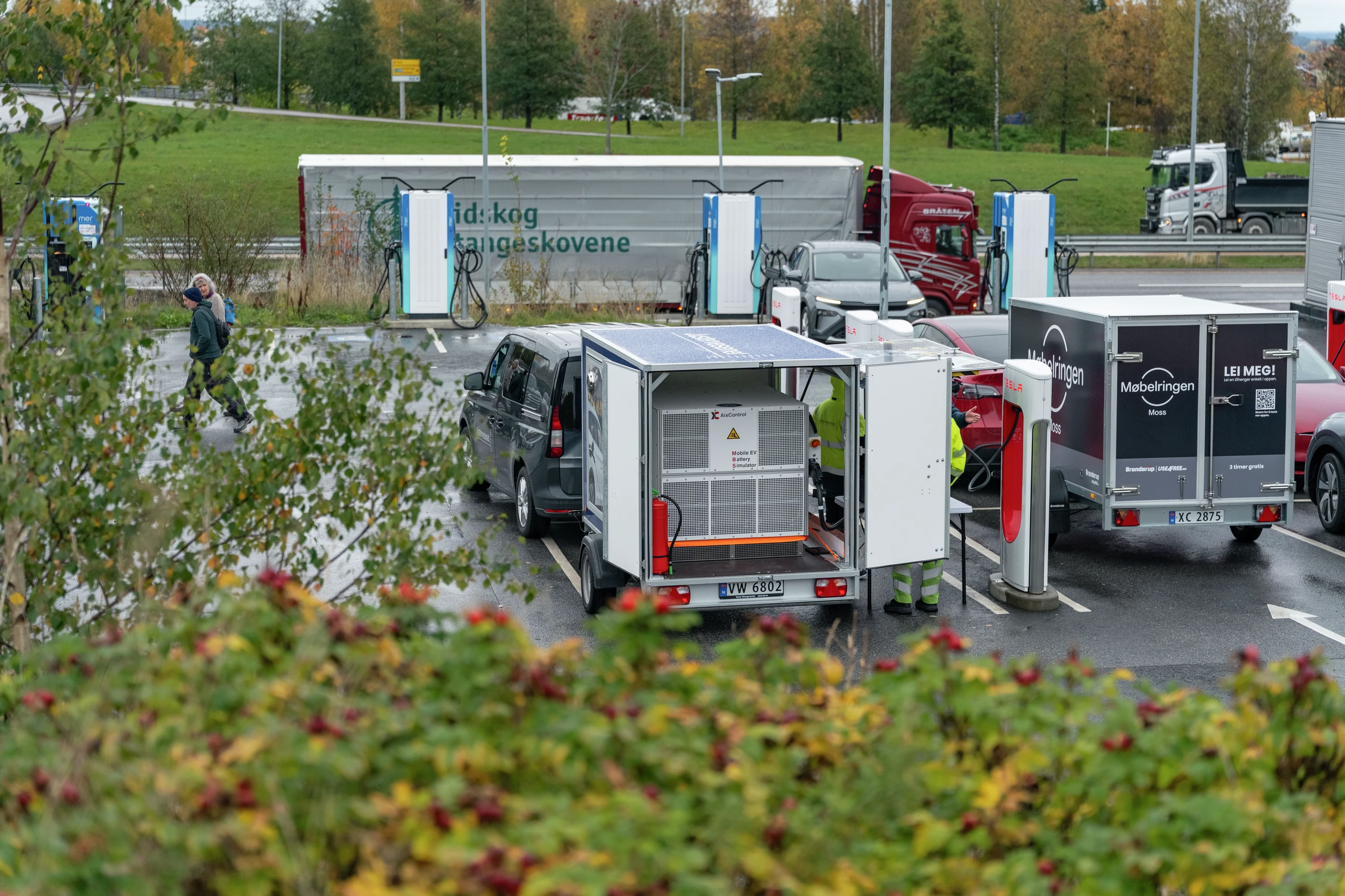 En travel ladestasjon for elbiler i Norge med flere kjøretøy, ladeenheter og en mobil batterihenger på en regnværsdag.