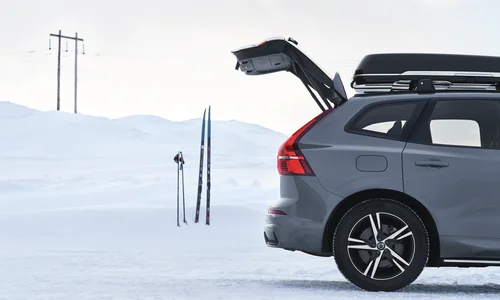 Grå Volvo XC60 med takbox och öppen baklucka står parkerad i vinterlandskap