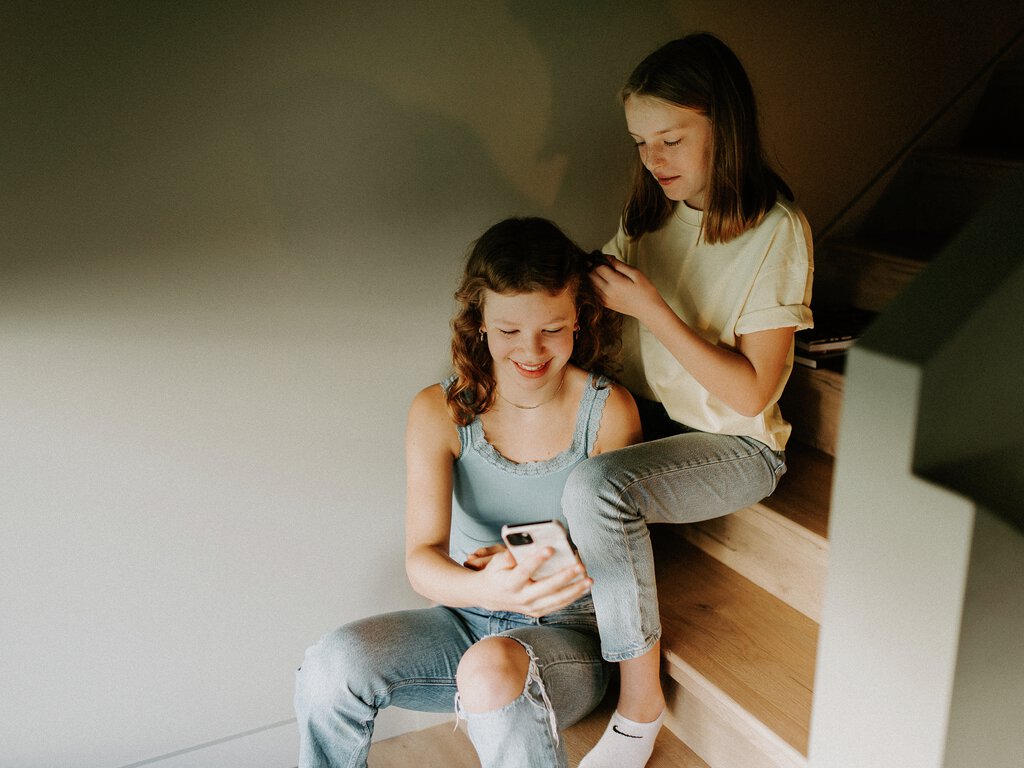 To jenter sitter i en trapp og fletter hår