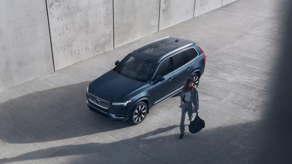 Kvinna går förbi en mörk Volvo XC90.