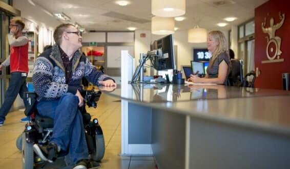 Mann i rullestol henvender seg til kvinnen i Ulobas resepsjon
