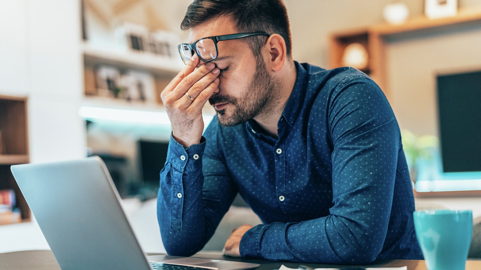 En mann som sitter foran en laptop og ser sliten og stresset ut