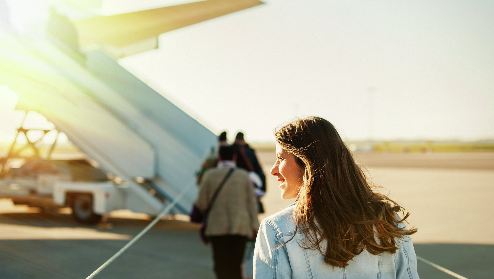 Moteris šypsosi eidama su kitais keleiviais link lėktuvo