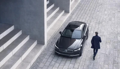Man passerar svart Volvo S90 som står parkerad vid en stentrappa.