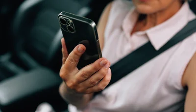 Kvinna sitter i bilen med säkerhetsbältet på och tittar i mobilen.