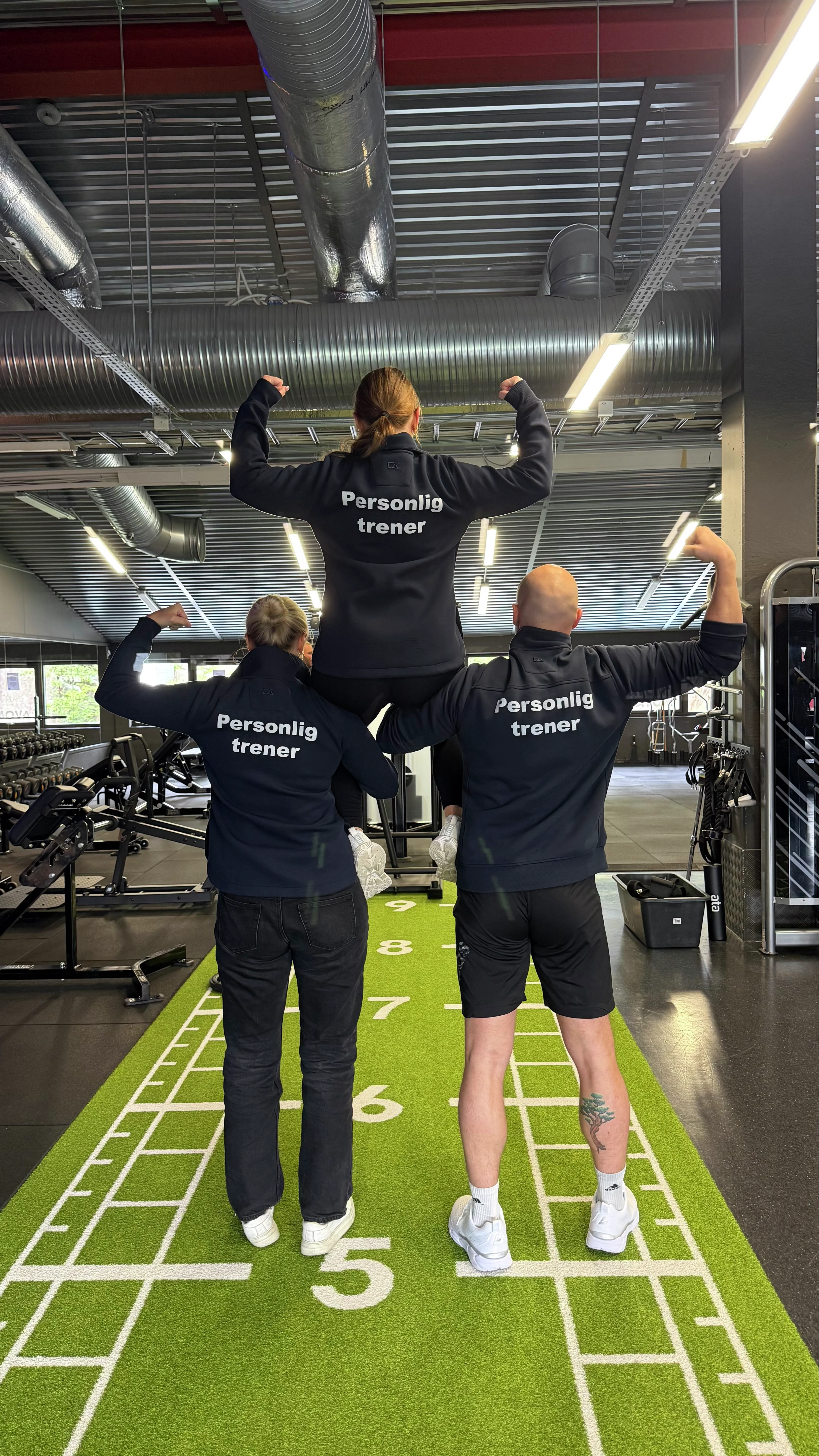 Tre personlige trenere sett bakfra på turfbanen, én løftet opp på skuldrene, på MOVA Mathopen.