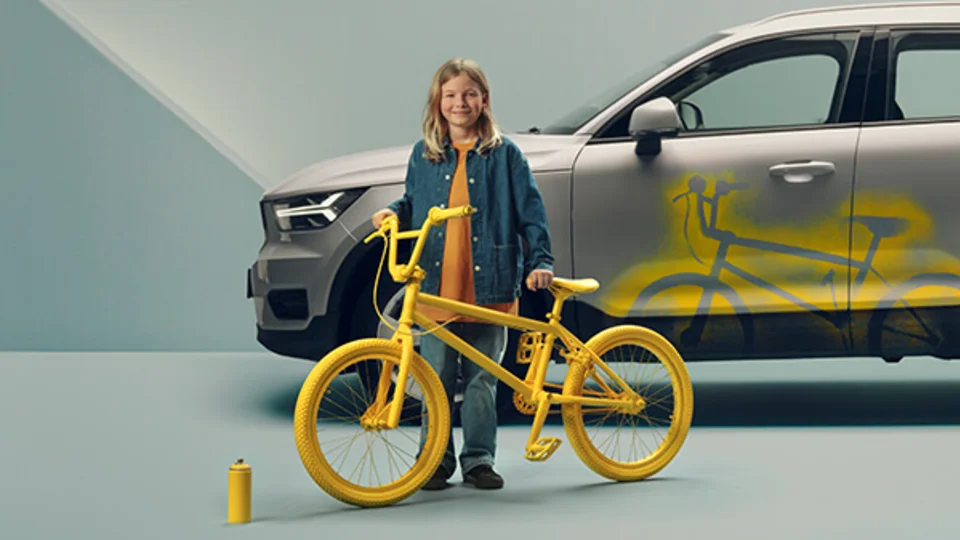 Barn står med spraymålad gul cykel vid en bil som har sprayfärg på sig.