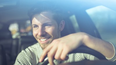 Hymyilevä mies istuu auton ratissa.