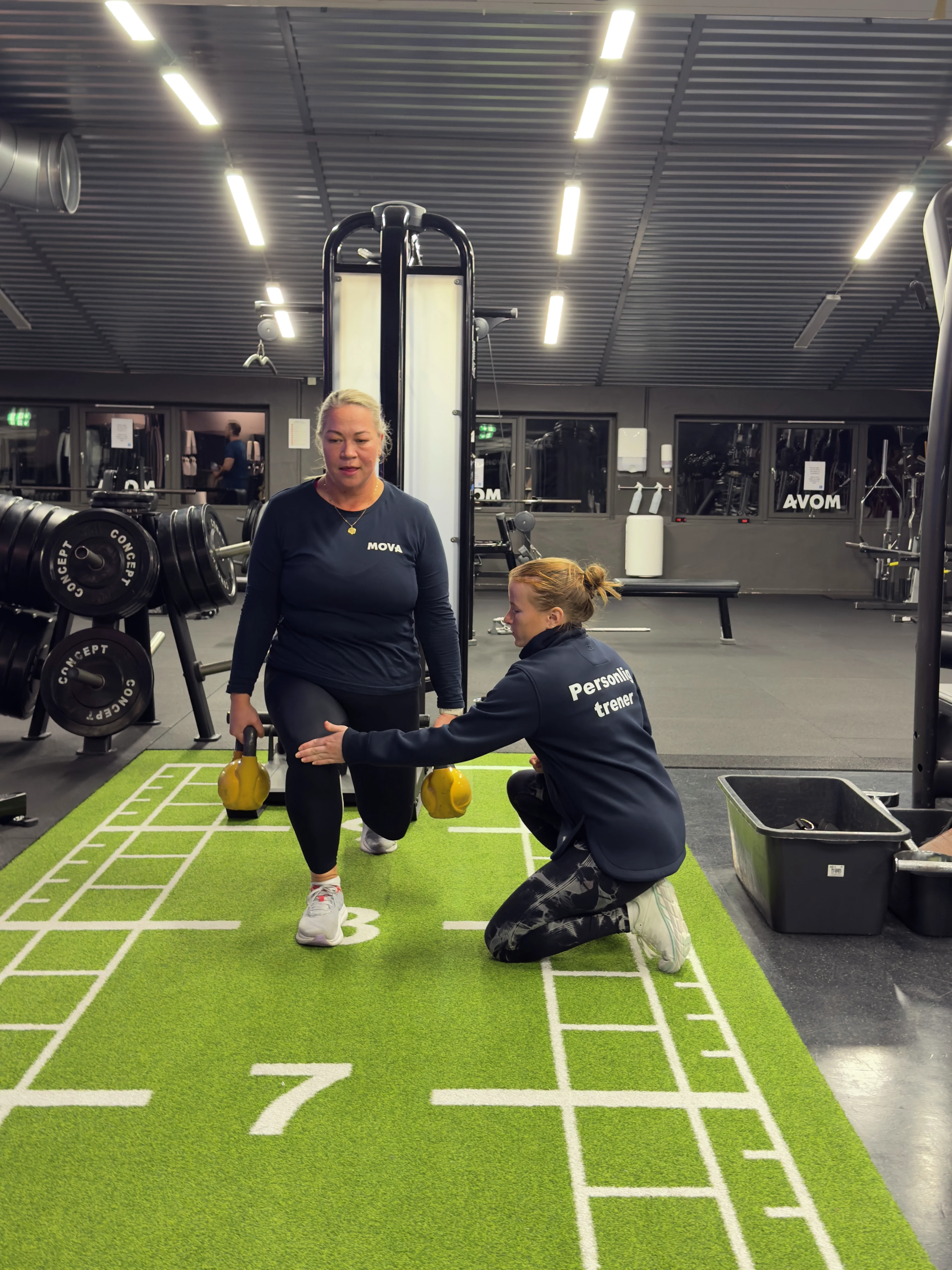 Personlig trener veileder en kvinne i utfall med kettlebells på turfbanen på MOVA Mathopen.