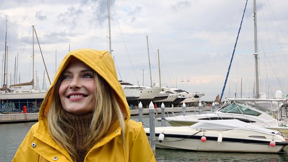 Nainen seisoo venesatamassa keltainen sadetakki päällään