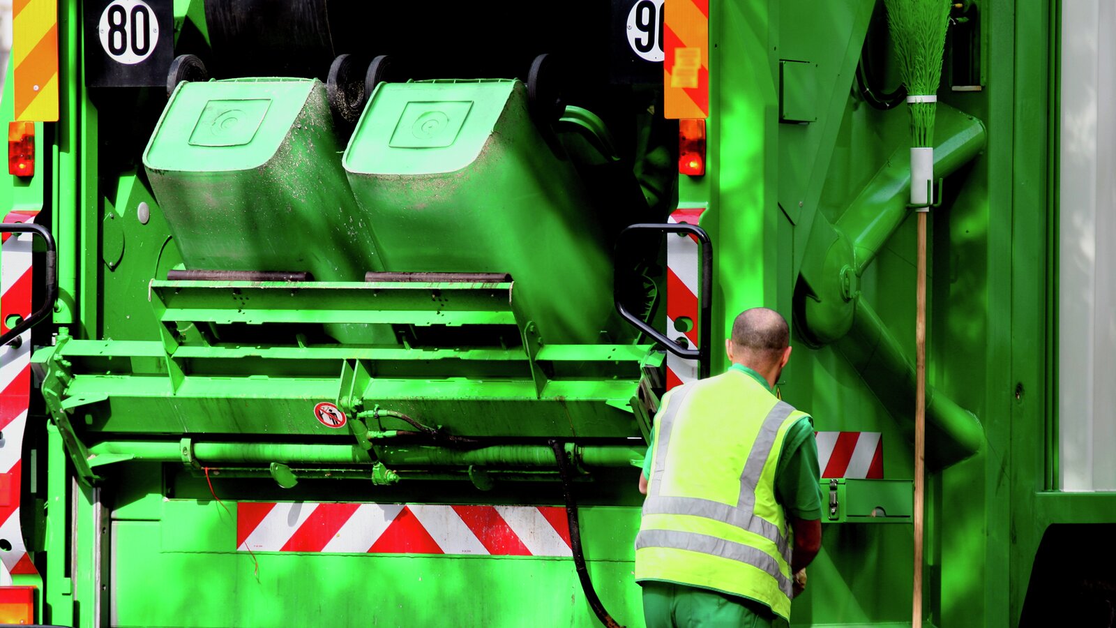 Grønn avfallsbil som tømmer 2 avfallsdunker