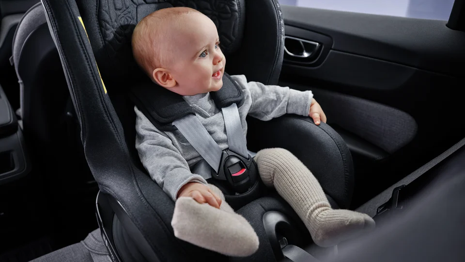 Leende bebis sitter i bakåtvänd bilbarnstol.