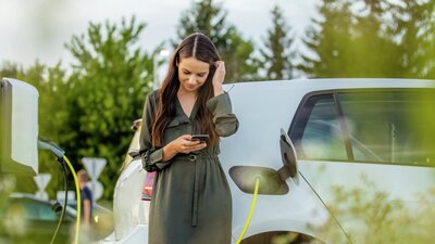 Kvinne står ved en elbil med en telefon i hånden