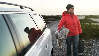 Nainen seisoo luonnossa sähköautonsa vieressä
