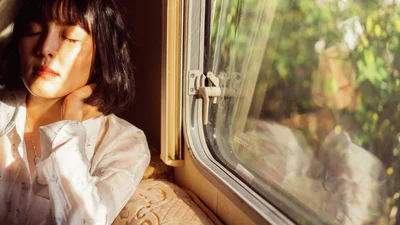 Nainen istuu aurinkoisessa junavaunussa silmät suljettuna