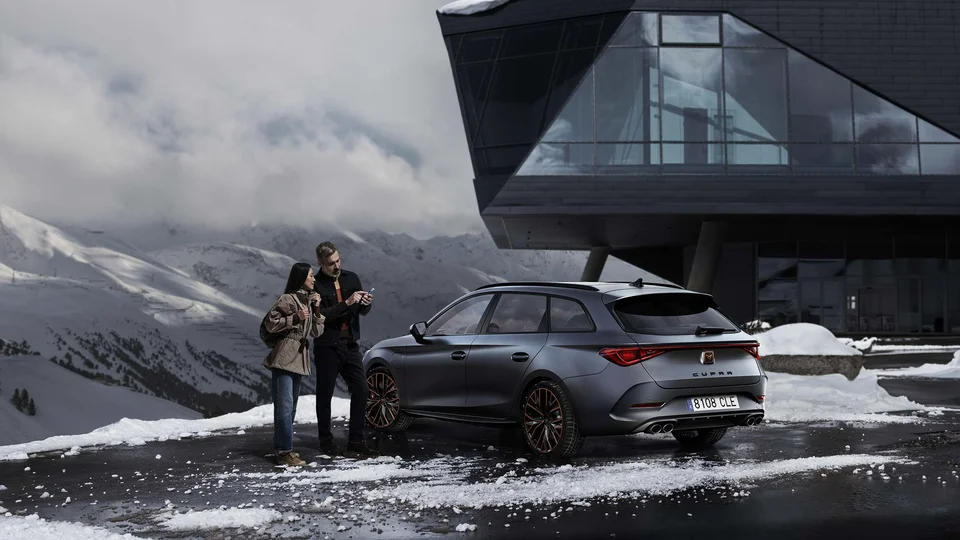 Par står vid en mörk bil omgiven av berg och snö.