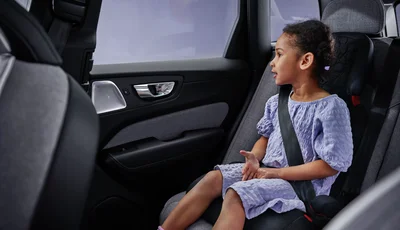 Flicka med lila klänning sitter i framåtvänd bilbarnstol.