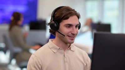 Ung mann sitter ved en PC og rådgir kunder på telefon