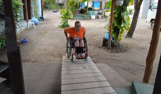 Mann i rullestol på vei opp rampe i stråhytte.