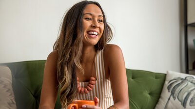 Nainen nauraa oranssi kahvikuppi kädessään