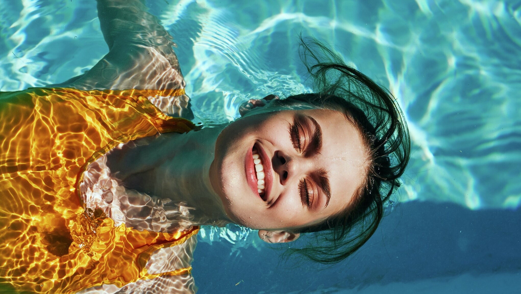 Moteris šypsosi plaukdama ant nugaros mėlyname baseine
