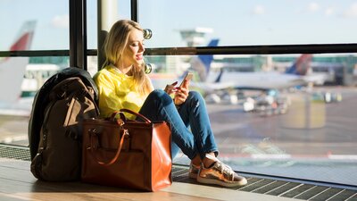 Nainen istuu lentokentän lattialla puhelin kädessä