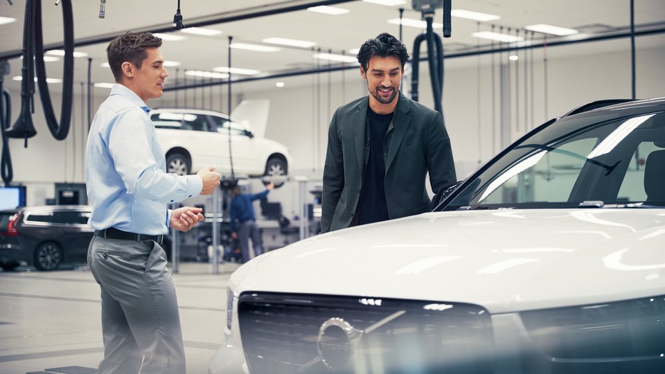 Två män tittar på en vit Volvo i en bilhall. 