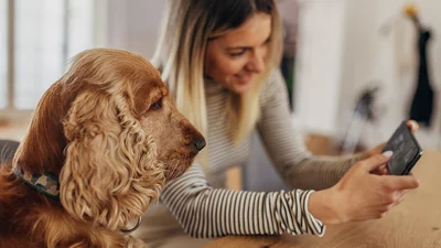 Kvinne og en hund sitter og ser på en mobil sammen
