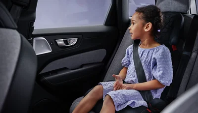 Flicka med lila klänning sitter i framåtvänd bilbarnstol.