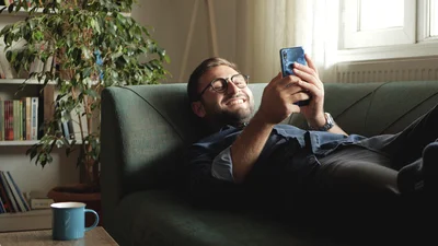 Ung mann ligger på sofaen med en mobil
