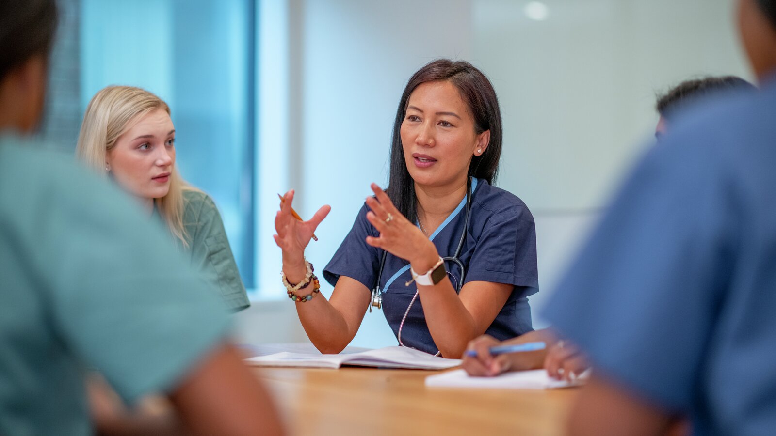 Sykepleier snakker til andre sykepleiere som sitter rundt et bord