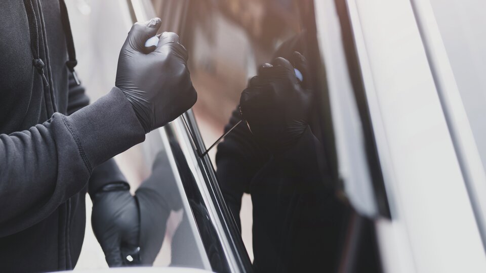 Person med svarta latexhandskar gör inbrott i bil via bilrutan