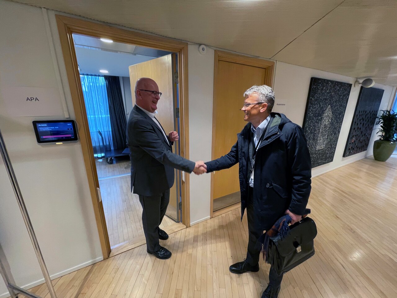 Statens personaldirektør, Gisle Norheim tar LO Stats leder Egil André Aas i hånda utenfor et møterom