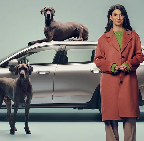 Kvinna står framför Volvo V60 tillsammans med två hundar, varav den ena hunden ligger på biltaket.