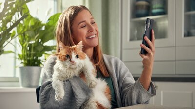 Nainen pitää kissaa sylissään ja katsoo puhelimen näyttöä