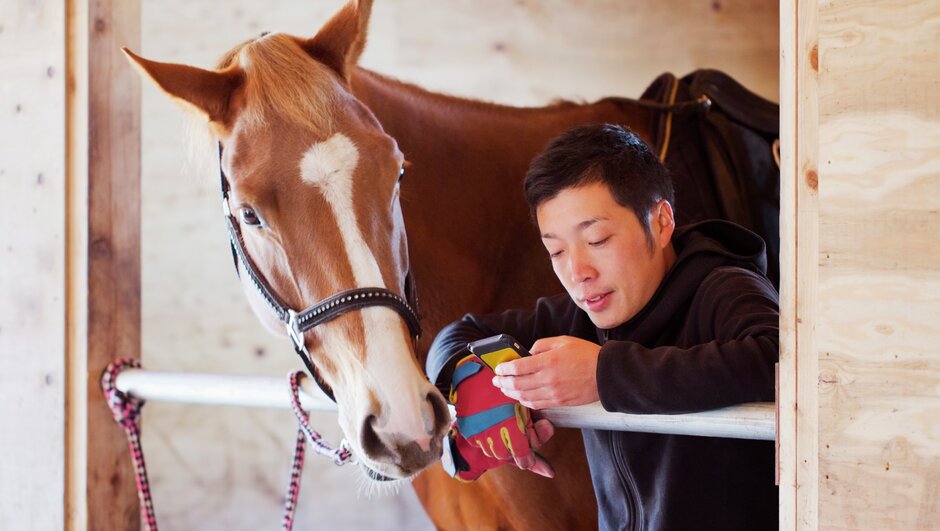 ung man står bredvid häst och har videosamtal med veterinär