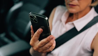 Kvinna sitter i bil och tittar på sin mobiltelefon.