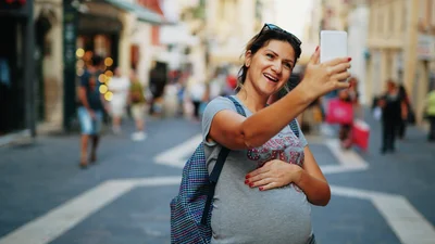 Gravid kvinna står på en gata och tar en selfie.