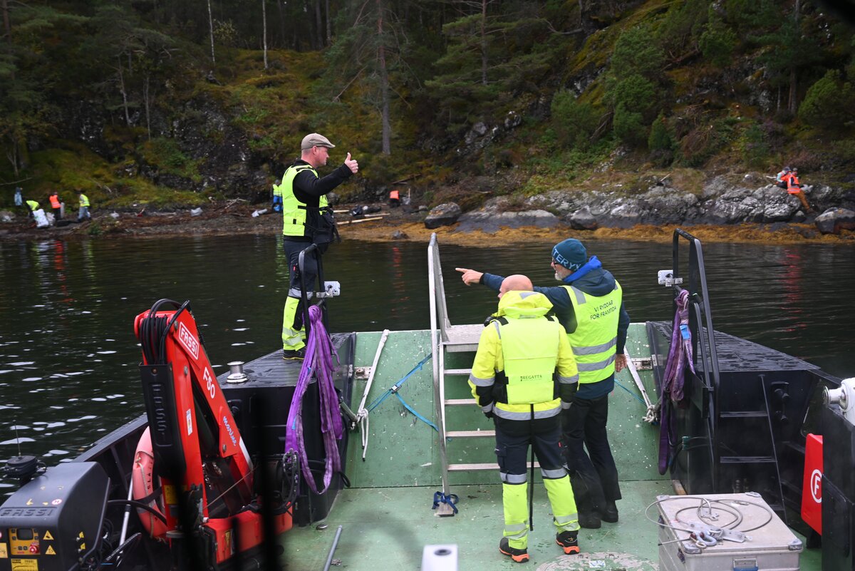 Folk i sikkerhetsutstyr på en båt som utfører forskning eller kartleggingsarbeid i en rolig fjord eller innsjø.