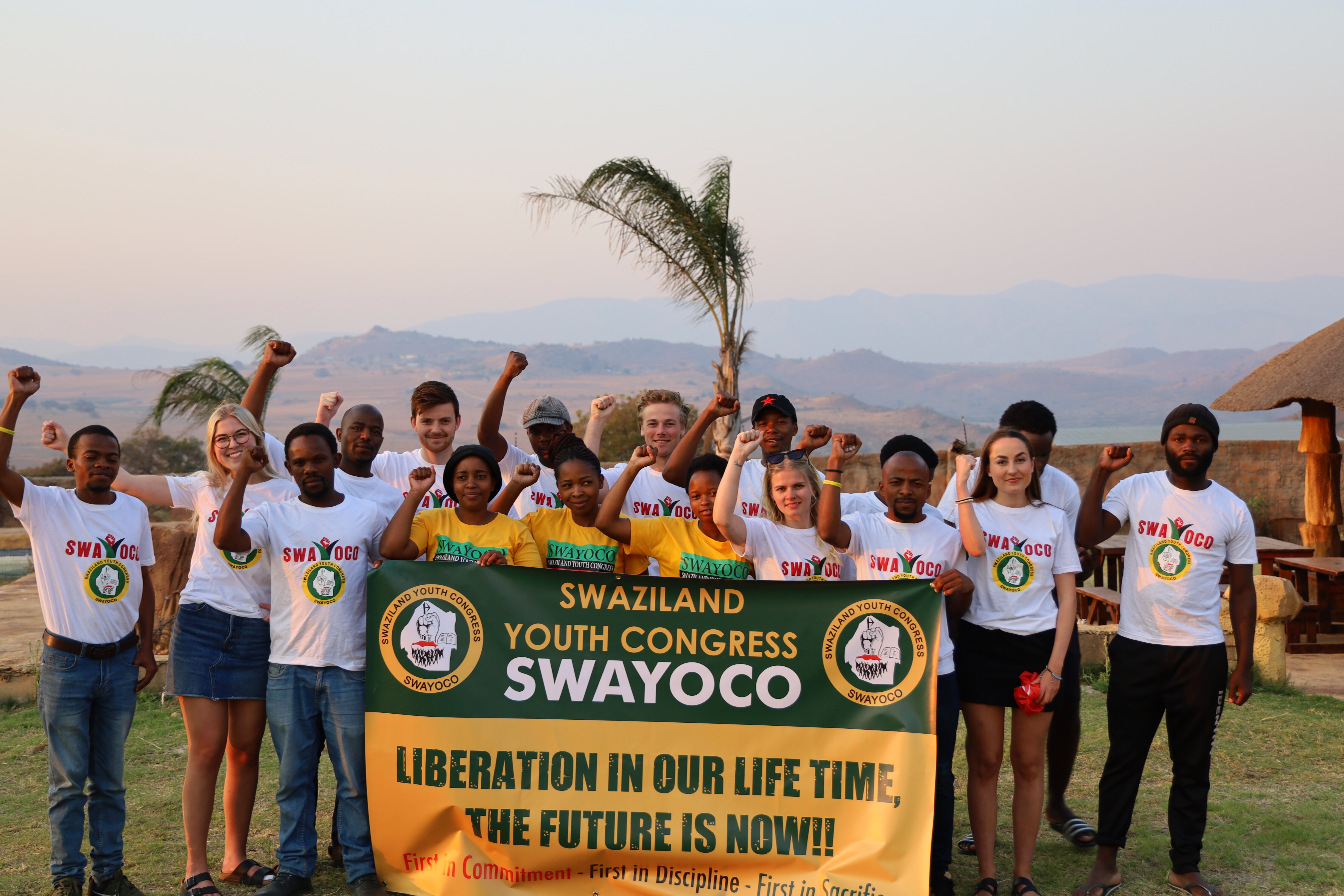 Gruppe med unge mennesker står med knyttneven i været. Bildet er tatt i Sør-Afrika. Foran seg holder de en plakat som sier "Swaziland youth congress Swayoco. Liberation in our life time, the future is now!"