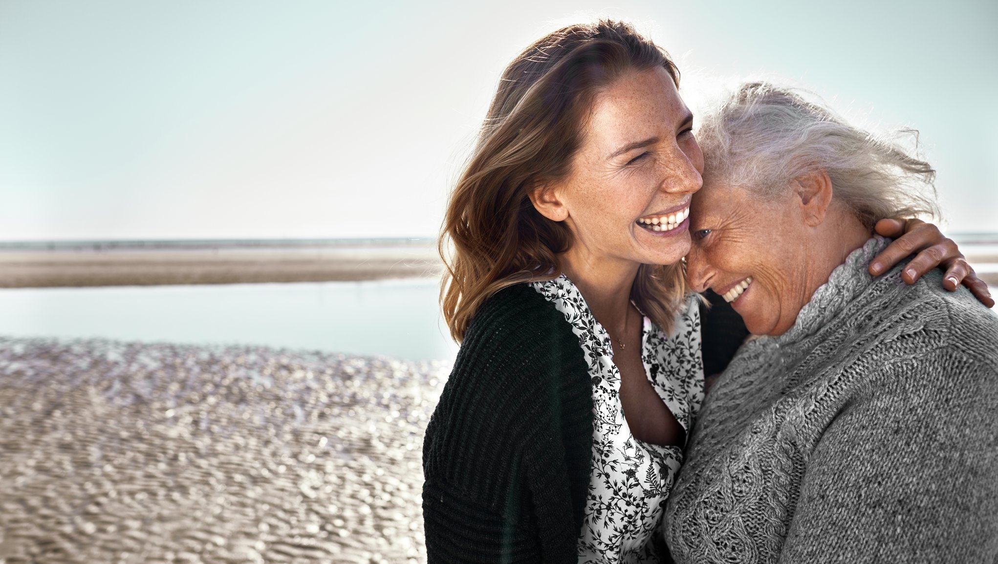 Nuori ja vanha nainen halaavat rannalla