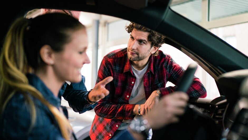 Ung man och kvinna tittar på bil hos en återförsäljare