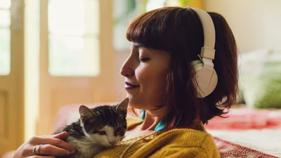 En kvinna sitter med hörlurar och katt i knä