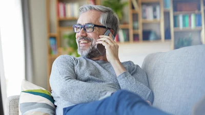 Mies istuu sohvalla ja puhuu puhelimeen