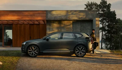 Volvo EX60 laddar utanför ett trähus.