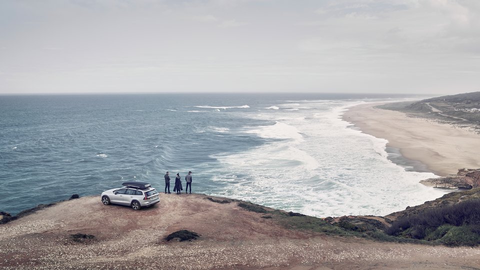Tre personer står framför vit Volvo V60 parkerad vid havet