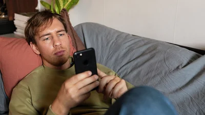 En ung mann ligger på sofaen og ser på mobilen