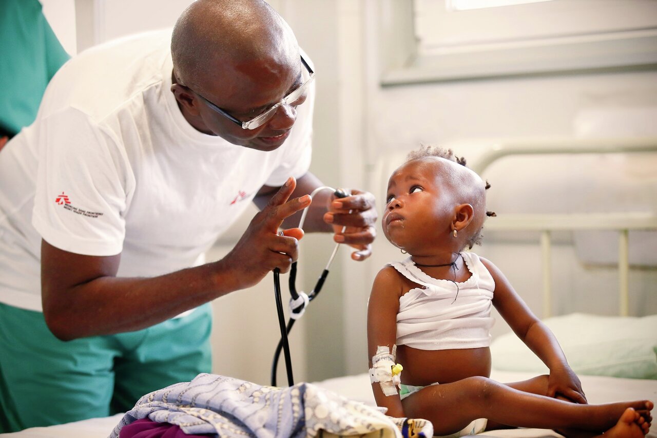 En lege som kommuniserer med en liten jente som sitter på sykehussengen