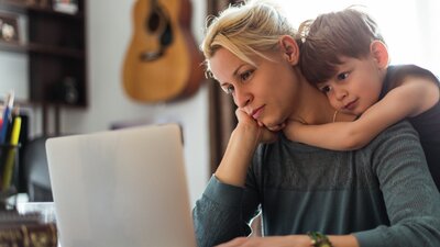 Nainen istuu tietokoneella lapsen halatessa häntä