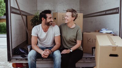 Mies ja nainen hymyilevät toisilleen muuttoautossa istuen